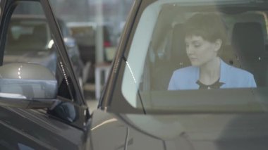 Formal giyim Mavi takım elbise giymek emniyet kemeri oturma arabanın motor show içine genç güzel kadın. Modern kız otomobil satın almak seçerek, titizlikle inceleniyor. Otomatik araç satın alma kavramı