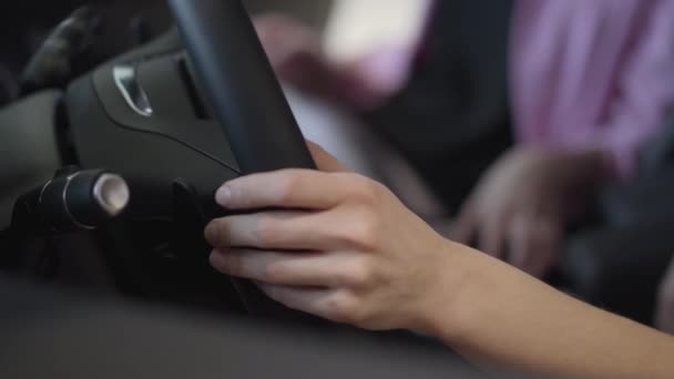 Una donna mette le mani sul volante grande da vicino. Ragazza moderna che sceglie l'automobile nel Motor Show. Concetto di acquisto di automobili, auto d'affari. Macchina fotografica si muove a destra — Video Stock