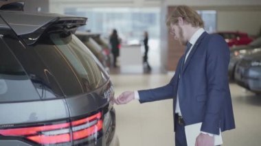 Sakallı işadamı araba motor seçimi kadar yakın göster. Uzun boylu adam tablet holding gövde açar ve araç inceler. Ciddi adam motor Show'da otomobil seçimi. Konsept araba satın alma