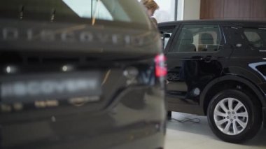 Resmi mutlu çift satırları seçmek için Otomobil Fuarı yeni araçların arasında yürüyüş giyinmiş. Araba ön bagajda. Konsept otomobil, otomatik iş satın alma