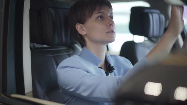 Formal giyim mavi genç güzel kadın portresi uygun yolcu koltuk önünde araba içinde oturuyor. Modern kız otomobil satın almak seçerek, motor gösterisinde incelenmesi. Kamera hareketleri doğru — Stok video