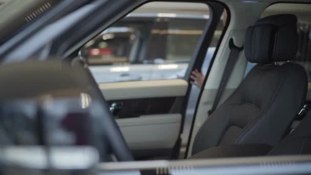 Mujer bonita joven en traje azul formal de desgaste abre la puerta del coche y se sienta dentro de ella en el asiento delantero del pasajero. Chica moderna examinando el interior del automóvil. Concepto de compra de un vehículo en el Salón del Automóvil — Vídeo de stock