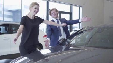Erkek ve kadın formal giyim modern Otomobil Fuarı araba aldım. Heyecanlı ve mutlu bir kadındır, otomobil, hugs gülümseyerek. İşadamı karısı için satın alma aracı