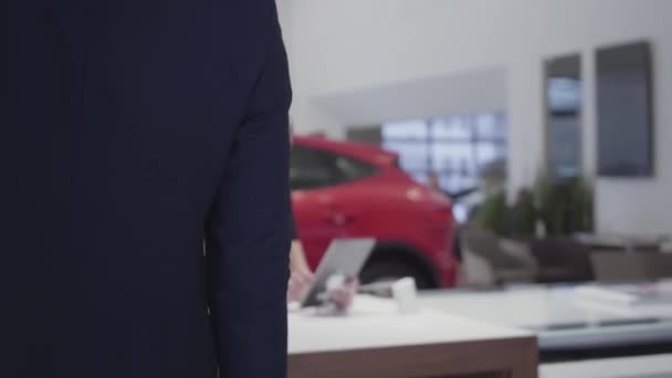 Tall man komt aan vertrouwen verkoper vrouw zitten aan de tafel. Vrouw geeft informatie aan man klant op tablet in moderne Autosalon. Verkoopster werken in auto showroom — Stockvideo