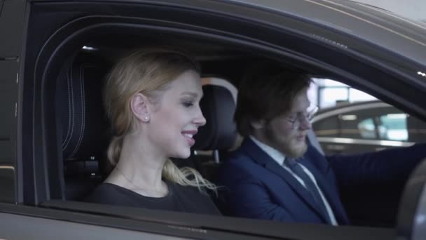 Χαρούμενα επιτυχημένο ζευγάρι κάθεται στο θάλαμο επιβατών του νέου οχήματος ελέγχει το εσωτερικό του το νεοαποκτηθέντα auto από την αντιπροσωπεία. Εκθετήριο αυτοκινήτων. — Αρχείο Βίντεο