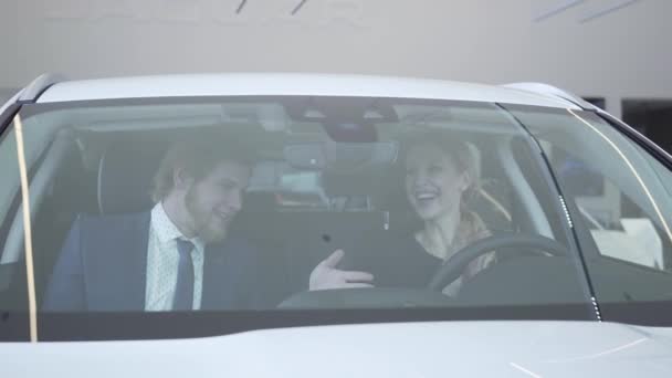 Joyeux couple assis à l'intérieur de la voiture qu'ils viennent d'acheter dans le salon de l'automobile moderne. Homme et femme à cinq, ils sont pleins d'émotions positives. Concept d'achat d'un véhicule — Video