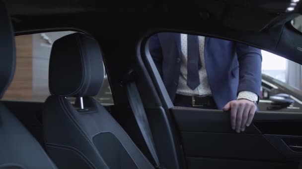 आधुनिक डीलरशिपमध्ये कारजवळ उभे असलेले सूट मध्ये अज्ञात व्यापारी विश्वासू माणूस कार शोरूममध्ये ऑटोमोबाईलची तपासणी करतो. ऑटो खरेदीची संकल्पना . — स्टॉक व्हिडिओ