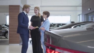 Yakışıklı sakallı satıcı iş takım elbiseli iki başarılı genç kız yeni bir oto hakkında bilgi bir araba Bayilik söyler. Araç Edilmesidir.