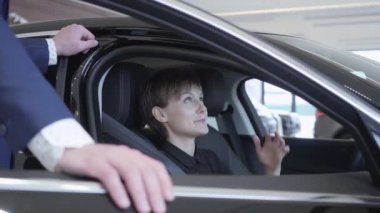 Modern araba tanınmaz satıcısıyla konuşmayı kısa saçlı sevimli genç kadın oturuyor. Başarılı kadın yeni otomatik inceliyor. Professioal satıcı müşteri danışmanlık takım elbiseli. Satın alma kavramı
