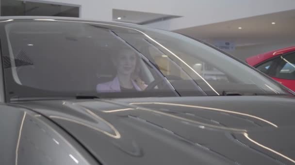 Feliz linda chica joven en el compartimiento de pasajeros del coche nuevo. La chica está llamando a un gerente de coche. concesionario de coches . — Vídeos de Stock