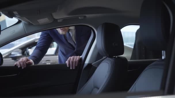 Uomo d'affari irriconoscibile in tuta guarda dentro auto, poi apre la porta e bella donna si siede dentro auto per esaminarlo. Concetto di acquisto di auto in showroom auto. Concessionaria auto . — Video Stock