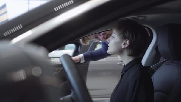 Jonge vrouw onderzoekt nieuwe auto zittend in de passagiersruimte van de nieuwe auto in auto showroom. Automobielbedrijf. — Stockvideo