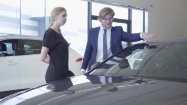 İş elbiseli gülen sakallı satıcı araba bayilik başarılı iş kadına yeni Auto gösteren. Showroom
