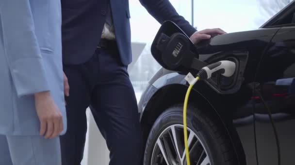 Senior branche le cordon d'alimentation à une voiture électrique. Caméra se déplace vers la gauche . — Video