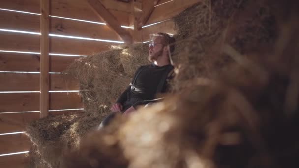 Knappe bebaarde man in glazen ademhaling ademt een wolk van stoom zittend op het hooi. Jonge boer rust na de werkdag in de schuur — Stockvideo