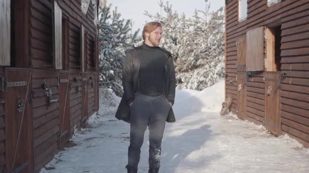 Retrato de um cara barbudo de óculos vestido com uma camisola quente e jaqueta larga. O tipo sorri e olha em volta. Movimento lento . — Vídeo de Stock