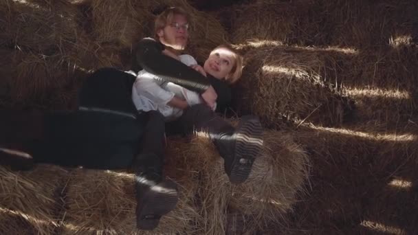 Beau barbu à lunettes et jolie femme allongée sur le foin dans la froide grange d'hiver. Joyeux couple de ranchers. Mouvement lent — Video