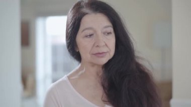Yumuşak hoş gülümseme ile kapalı etrafa muhteşem uzun siyah saçlı çekici kadın kıdemli portresi kapatın. Arka plan bulanık