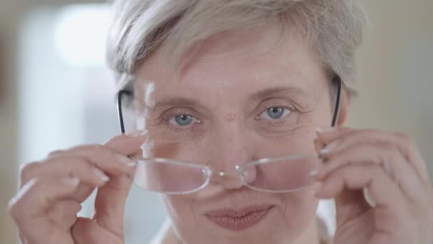 Retrato de una mujer madura de pelo blanco con gafas y mirando de cerca a la cámara . — Vídeos de Stock