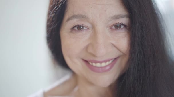 Ritratto di attraente donna anziana con splendidi lunghi capelli scuri e sorriso guardando in macchina fotografica al chiuso . — Video Stock