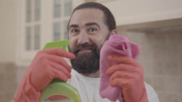 Портрет красивого чоловіка з ідеальною бородою посміхається і показує пральний порошок після прибирання всього свого нового сучасного будинку — стокове відео