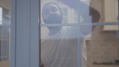 Hipster güzel çekici adamla sakal eldiven penceresinde yeni modern evinde deterjan ile Temizleme