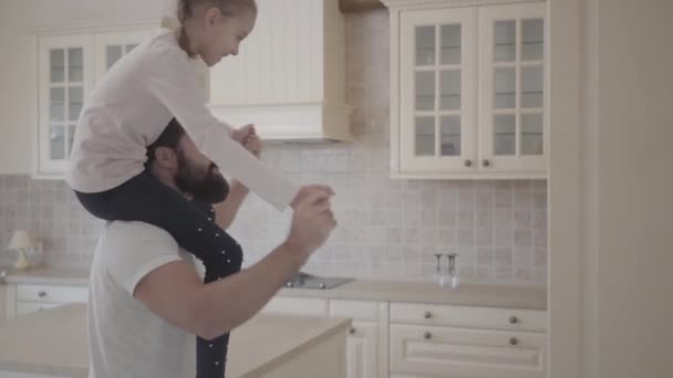 Gelukkig schattige dochter zittend op haar vaders schouders plezier torether op de prachtige moderne keuken. Vader en dochter relatie. Een gelukkige familie. — Stockvideo