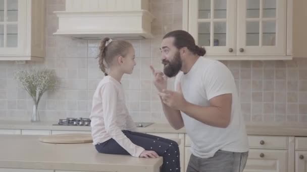 Jolie fille assise sur la table écoutant l'histoire émotionnelle de ses pères et s'amusant à s'asseoir sur la belle cuisine moderne. Relation père-fille . — Video