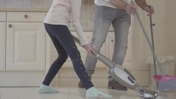 Dad and daughter having fun in a clean house. A man with broom and dustpan and girl with a vacuum cleaner. Pastime father and daughter together. Father and daughter relationship. A happy family. — Stock Video