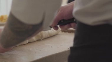Aşçı tek tip kesme hamur pizza için genç pizza Maker'da modern mutfak büyük bıçak elleri kapatın. Zeytinyağı, domates fesleğen ve peynir masanın üzerinde. Kamera hamle yaptı