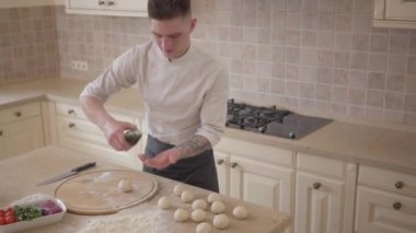 Genç pizza yapımcısı cook üniformalı zeytinyağı mutfakta pizza hamur topları yuvarlanma taraftan dökülen. Gıda hazırlama kavramı. Yukarıdan çekim Üstten Görünüm