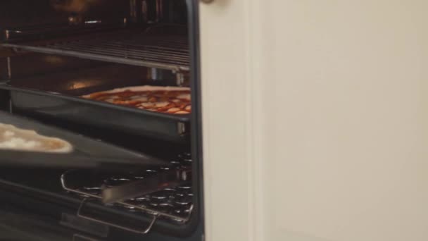 Mano de cocinero poniendo pizza en horno eléctrico de cerca. Hombre colocando pizza en una bandeja para hornear dentro de la cocina caliente. Preparación de alimentos, platos caseros. Cámara se mueve derecha e izquierda — Vídeo de stock