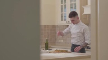 Üniformalı profesyonel şef pizza evde mutfakta yapar. Şef rendelenmiş parmesan peynirli pizza sıralar. Boyutu görüntüleyin. Pişirme kavramı.