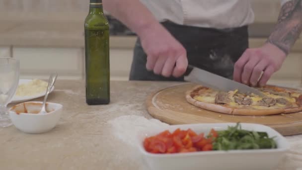 Close up de mãos de homem irreconhecíveis cortando sua pizza em pedaços com uma faca grande. Conceito de preparação de alimentos. Câmara se move para a direita — Vídeo de Stock