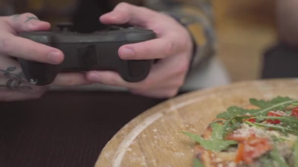 Close-up van handen van twee jonge mannen spelen video spel bedrijf joystick in handen thuis. Pizza met tomaten en rucola in de voorgrond op tafel liggen. Vrije tijd voor vrienden — Stockvideo