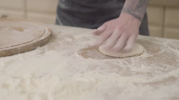 Cierre las manos de un joven fabricante de pizza en delantal preparando la masa usando un rodillo de masa en casa. Concepto de preparación de alimentos. Cámara se mueve derecha — Vídeo de stock