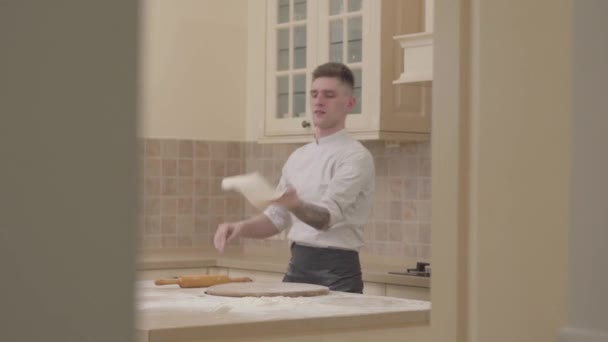 Professional cook spinning and throwing pizza dough up in the air with two hands in kitchen. — Stock Video