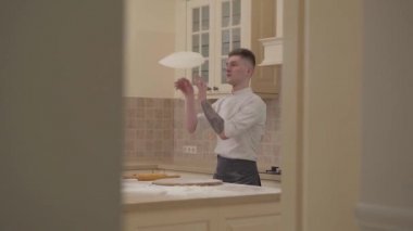 İplik ve pizza hamuru iki havayla yukarı atma genç adam yan görünüm mutfakta eller. Ağır çekim.