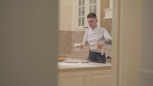 Медленное движение красивого молодого человека, крутящегося и выбрасывающего тесто для пиццы — стоковое видео