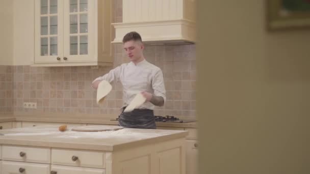 Ung kille spinning och gungade två diskar av pizzadeg i köket hemma. Professionell pizzaiolo att göra pizza. Begreppet beredning av livsmedel. Slow motion. — Stockvideo