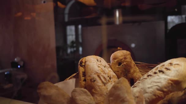 Pão recém-assado deitado na cesta em primeiro plano sobre a mesa no restaurante moderno de perto. Forno com fogo ardente no fundo — Vídeo de Stock