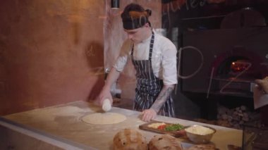Usta pizza makinesi hamur modern restoran mutfak cam arkasında at yemek pişiriyor. Adam pizza hamur ürünleri için form üzerinde süt dökülen. Pizza pişirme işlemi