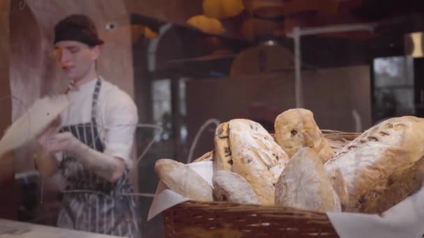Frisch gebackenes Brot, das im Korb im Vordergrund auf dem Tisch in einem modernen Restaurant in Großaufnahme liegt. Profi-Koch dreht und wirft Pizzateig in Restaurantküche hoch. — Stockvideo