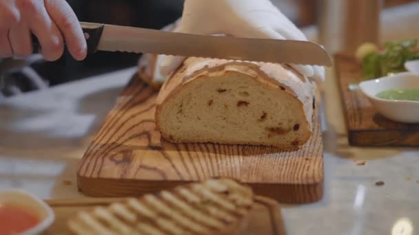 Mani di chef in guanti di gomma bianca che tagliano il pane di grano sul tagliere di legno da vicino. Servizio di cibo in ristorante moderno — Video Stock