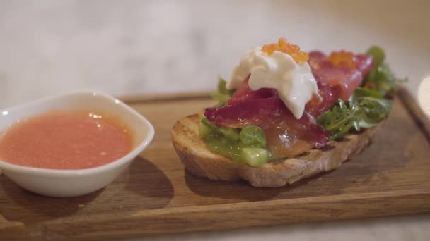 Aperitivo de pão delicioso com peixe vermelho, creme e caviar vermelho em uma placa de cozinha de madeira close-up . — Vídeo de Stock