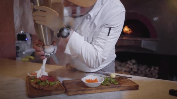 Sandwich with arugula and salted salmon is cooking in restaurnt close up. Unrecognizable chef making tasty food for serving on wooden board. Cook putting cream from big borrle and caviar on the top — Stock Video