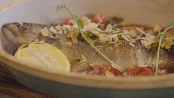 레몬, 체리 토마토, 채소, 견과류와 함께 장식 하는 깊은 접시에 누워 신선한 구운된 생선의 보기를 닫습니다. 현대적인 레스토랑, 바다 음식에에서 봉사 하는 음식 — 비디오