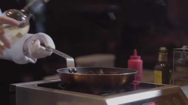 Mani di chef in guanti di gomma bianca versano il vino bianco nella padella, cucinando gustoso piatto in ristorante moderno da vicino. Processo di preparazione degli alimenti — Video Stock