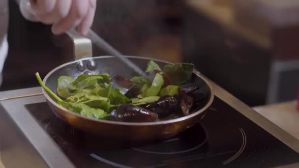 요리사 손 치찰음의 기름과 마늘 집게를 사용 하 여 프라이팬에 잎 홍합을 혼합 닫습니다. 레스토랑 주방에서 준비 해산물 — 비디오
