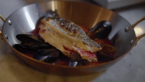 Vis filet liggen in diepe aluminium pan met handvaten met rode saus binnen met mosselen met kruiden, peper en zout beregening close-up. Voorbereiding zeevruchten in restaurant keuken — Stockvideo